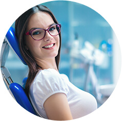 A young woman sitting in a dental chair smiling as she waits for her oral cancer screening to start