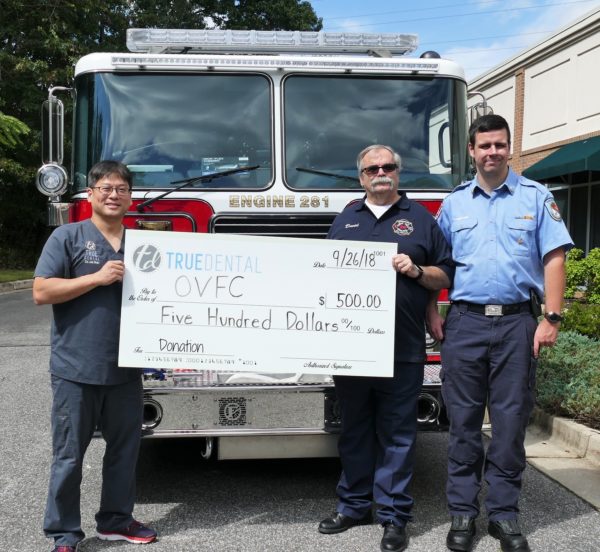 Dr. Shin with the Odenton Volunteer Fire Company holding a $500 check donation in front of a fire truck