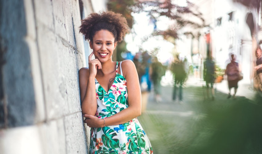 Curly-haired woman wearing a floral summer dress against a cement wall