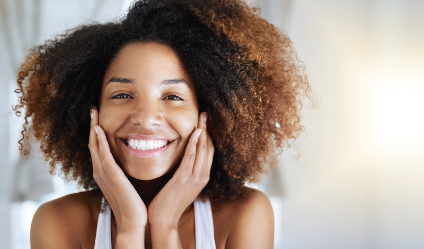 Curly-haired woman smiles brightly with a fully restored smile thanks to with dental implant tooth replacement