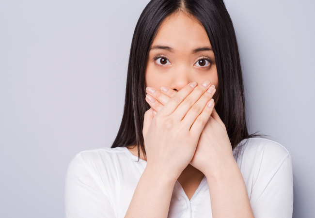 Brunette woman with bleeding gums covers her mouth with her hands in embarrassment