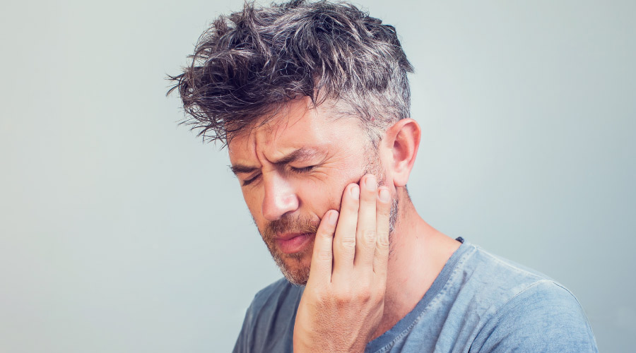 Middle-aged man cringes and touches his jaw due to jaw pain after waking up