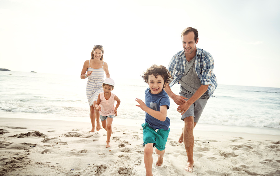 Mom, dad, son, and daughter smile as they run and play on the beach during the summer