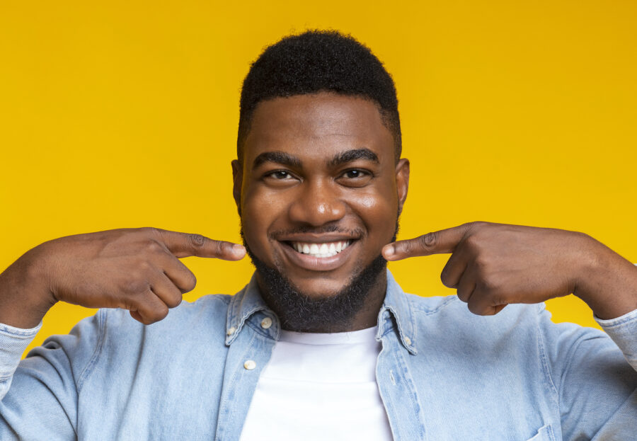 Black man smiles brightly and points to his teeth against a yellow background