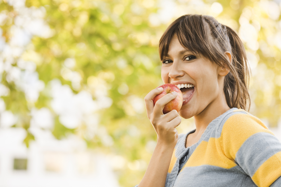 Outdoors portrait of a pretty girl eating an apple, natural ingredients for oral health